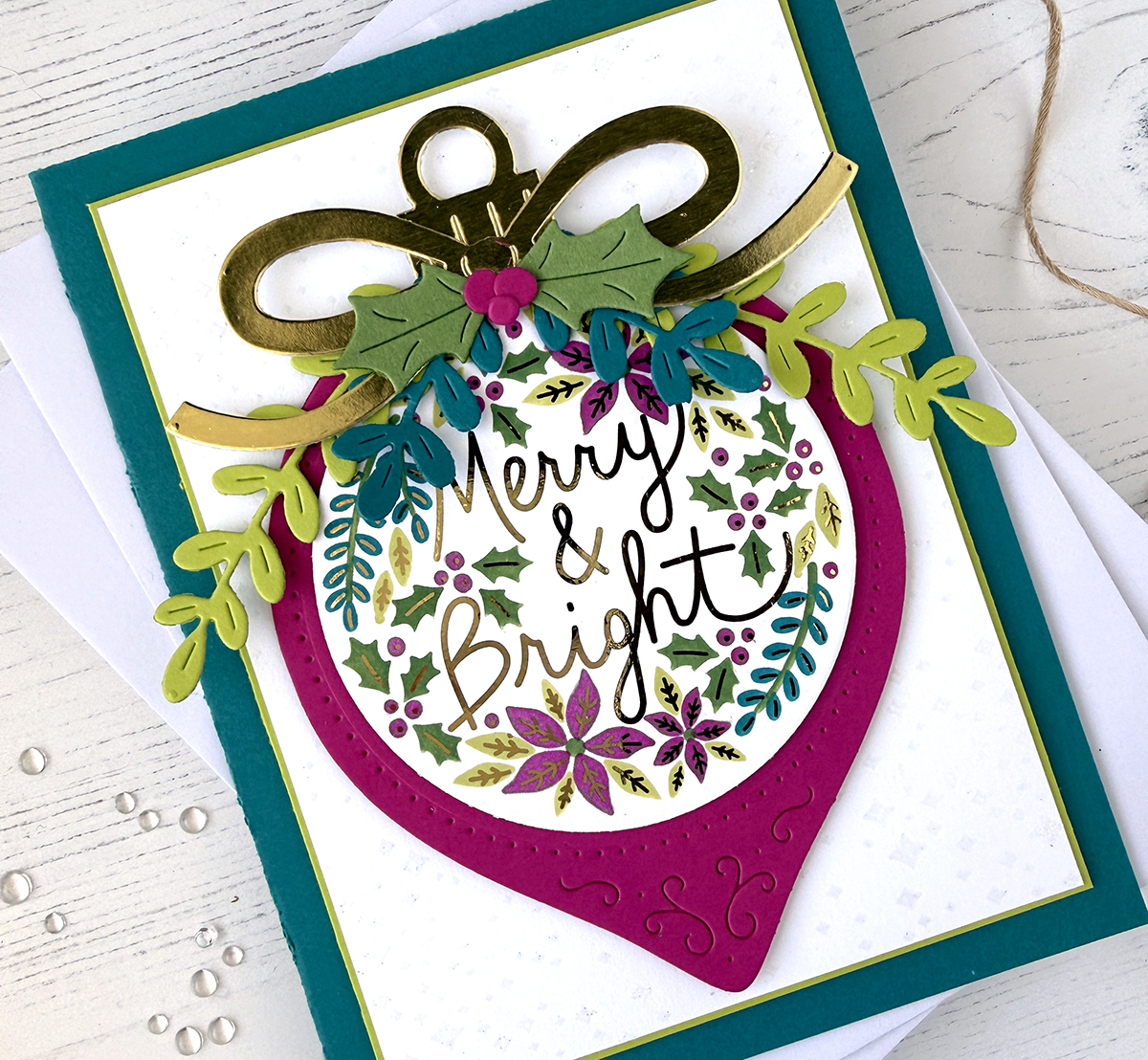 A photo of a brightly colored handmade card with a Christmas ornament on the front. The ornament is bright pink with Merry & Bright in gold metallic script.